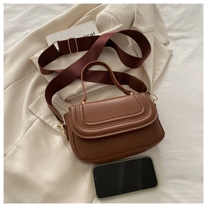 Detail of tan crossbody bag with wide strap and phone for scale on light jacket