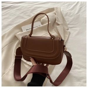 Detail of brown leather crossbody bag featuring wide red shoulder strap and gold hardware