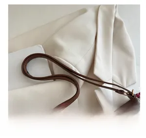 Détail de la fine bandoulière en cuir et de l'anneau en métal sur un sac cabas marron