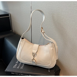 Détail du sac baguette crème avec fermoir doré sur un présentoir minimaliste