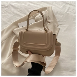 Detail of beige PU leather crossbody bag with curved flap and gold hardware accents