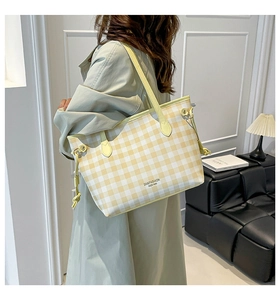 Detail of yellow and white plaid tote bag with shoulder strap worn over a trench coat