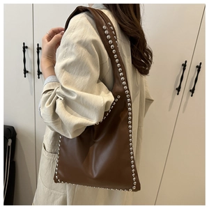 Close-up of brown leather hobo bag featuring silver rivet trim and shoulder strap detail