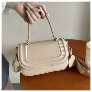 Detail of beige PU leather crossbody bag featuring gold hardware and wide woven strap