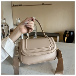 Detail of beige faux leather handbag featuring arc quilting and detachable woven strap
