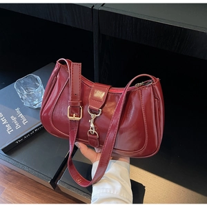 Détails d'un sac baguette bordeaux brillant avec boucle dorée et bandoulière réglable