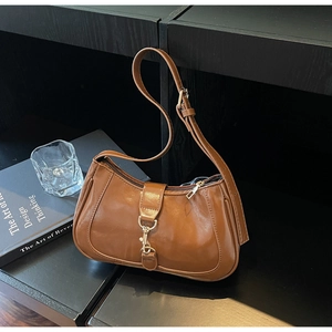 Détail d'un sac baguette en cuir marron brillant avec boucle en métal sur un présentoir noir