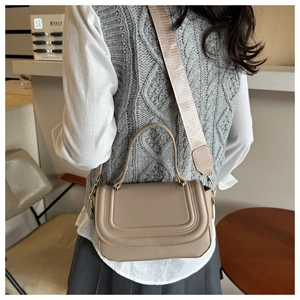 Chic beige crossbody bag with U-shaped stitching and wide fabric strap shown on a model