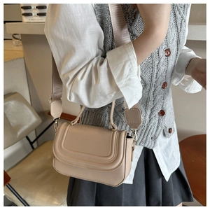 Detail view of khaki PU leather crossbody bag with stitching and wide strap in a cafe setting