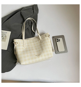 Detail of light beige checkered tote bag featuring gold lettering and side drawstring knot