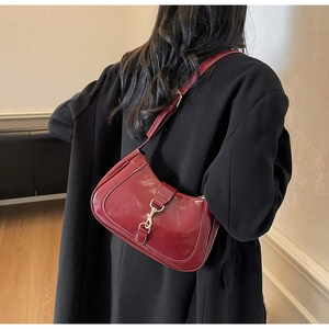 Détail du sac baguette rouge brillant avec boucle argentée porté à l'épaule par un mannequin