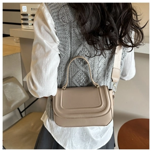 Minimalist beige crossbody bag with curved stitching and a wide fabric strap shown on model