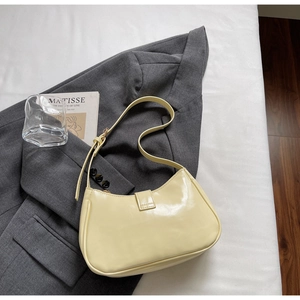 Détail d'un sac baguette beige verni montrant sa forme hobo et sa bandoulière réglable