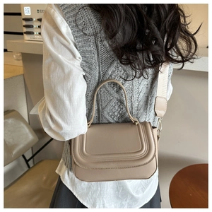 Detail view of a beige crossbody square bag with U-shaped quilting and wide woven strap