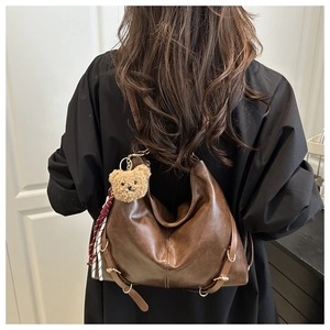 Détail d'un grand sac cabas en cuir marron avec pendentif ours et breloque tressée