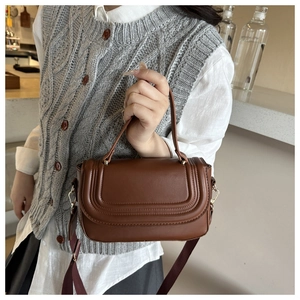 Close-up of brown leather crossbody bag featuring embossed lines and a wide textile strap