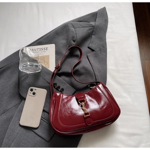 Gros plan sur le sac bandoulière en cuir verni bordeaux avec finitions dorées chic