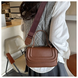 Detail of a brown leather crossbody bag with a wide burgundy fabric strap on a model
