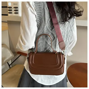 Detail of brown leather handbag with curved quilting and stylish wide fabric strap