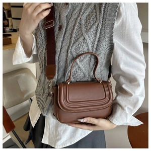 Close-up of brown leather crossbody bag with wide strap and moon flap detail