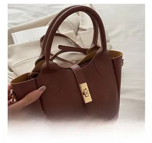 Détail d'un sac à main en cuir marron avec fermoir doré rotatif et poignée ergonomique