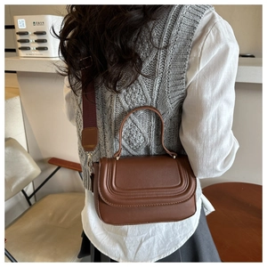 Detail of dark brown leather crossbody bag with embossed flap and wide red strap