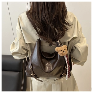 Détail du sac cabas en cuir marron foncé avec breloque ours porté sur un trench beige