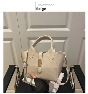 Détail du sac seau beige avec deux poignées, fermoir en métal et logo embossé chic