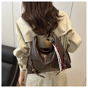 Détail du sac hobo en cuir marron vintage avec sangles latérales et accessoire pompon doux