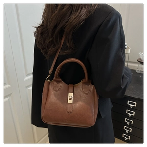 Sac bandoulière trapèze en similicuir marron avec fermoir doré porté par un mannequin