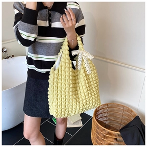 Detail of light yellow textured tote bag with a white lace bow on the shoulder handle