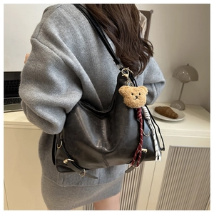 Grand sac hobo noir avec breloque ours, porté par un mannequin dans un intérieur chaleureux