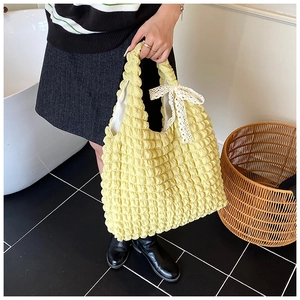Detail of pale yellow popcorn texture handbag featuring delicate white lace bow decor