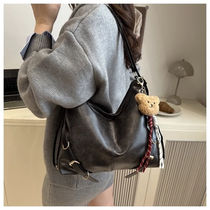 Détail du sac cabas en cuir noir vintage avec boucles latérales et breloque ours peluche