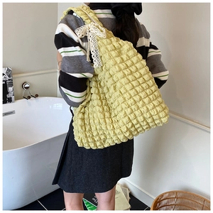 Detail of yellow pleated shoulder bag featuring a white lace bow and textured fabric