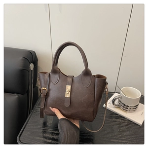 Détail du sac seau marron foncé avec fermoir doré et bandoulière dans un cadre élégant
