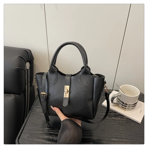 Détail d'un sac cabas en cuir PU noir avec fermoir doré sur une surface en bois sombre