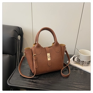 Détail du sac seau en cuir PU marron avec fermoir rotatif doré sur une table en bois