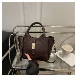 Détail d'un sac seau en cuir texturé marron foncé avec fermoir doré et bandoulière longue