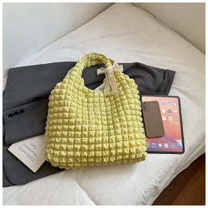 Detail of light yellow ruched puff shoulder bag with white lace bow and textured surface
