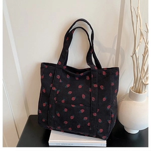 Detail of black corduroy tote bag featuring red strawberry patterns and front pocket
