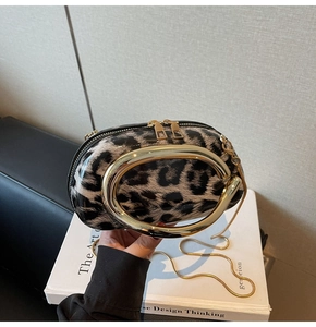 Detail of leopard print oval clutch bag with gold metal handle and chain on books