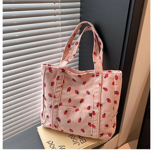 Dettaglio della borsa tote in velluto rosa con stampe di fragole sui libri