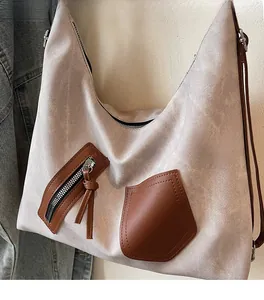 Detail of beige hobo bag showing brown leather zipper pocket and textured fabric finish