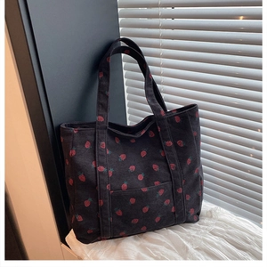 Dettaglio della stampa a fragola sulla borsa tote in velluto nero con luce soffusa