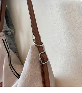 Close-up of beige canvas tote with brown leather strap and polished silver hardware detail