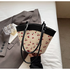 Detail of cream tote bag featuring red cherry print and black contrasting handles