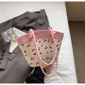 Close-up of a cream tote bag featuring red cherry prints and pink leather handles