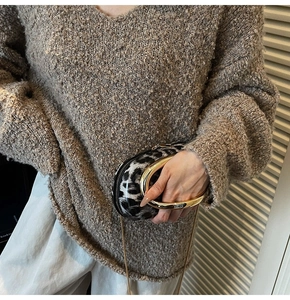Close-up of leopard print handbag with golden circular metal handle and slim chain strap