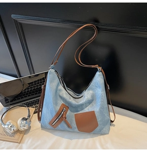 Large blue canvas tote bag with brown leather straps and front zipper pocket details